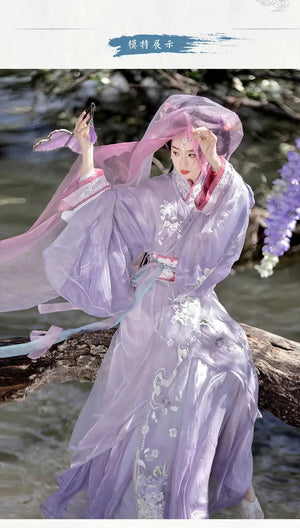 Woman in purple Hanfu sitting by water with veil