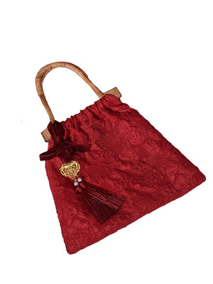 Isolated view of a red bridal handbag with floral texture, bamboo handle, and tassel embellishment. Perfect for elegant weddings.