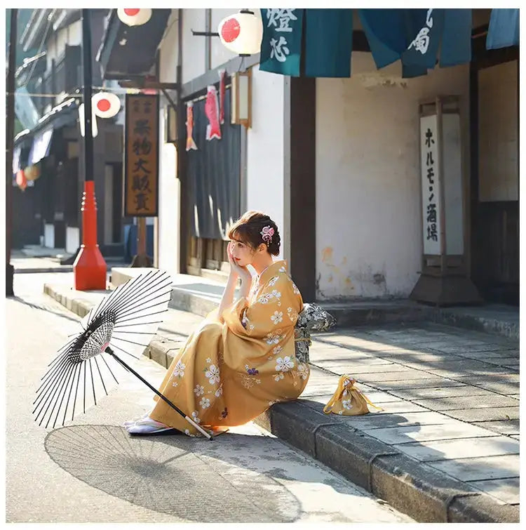 Woman in an orange floral kimono yukata sitting on a stone pavement, holding a traditional umbrella in a peaceful Japanese street setting.