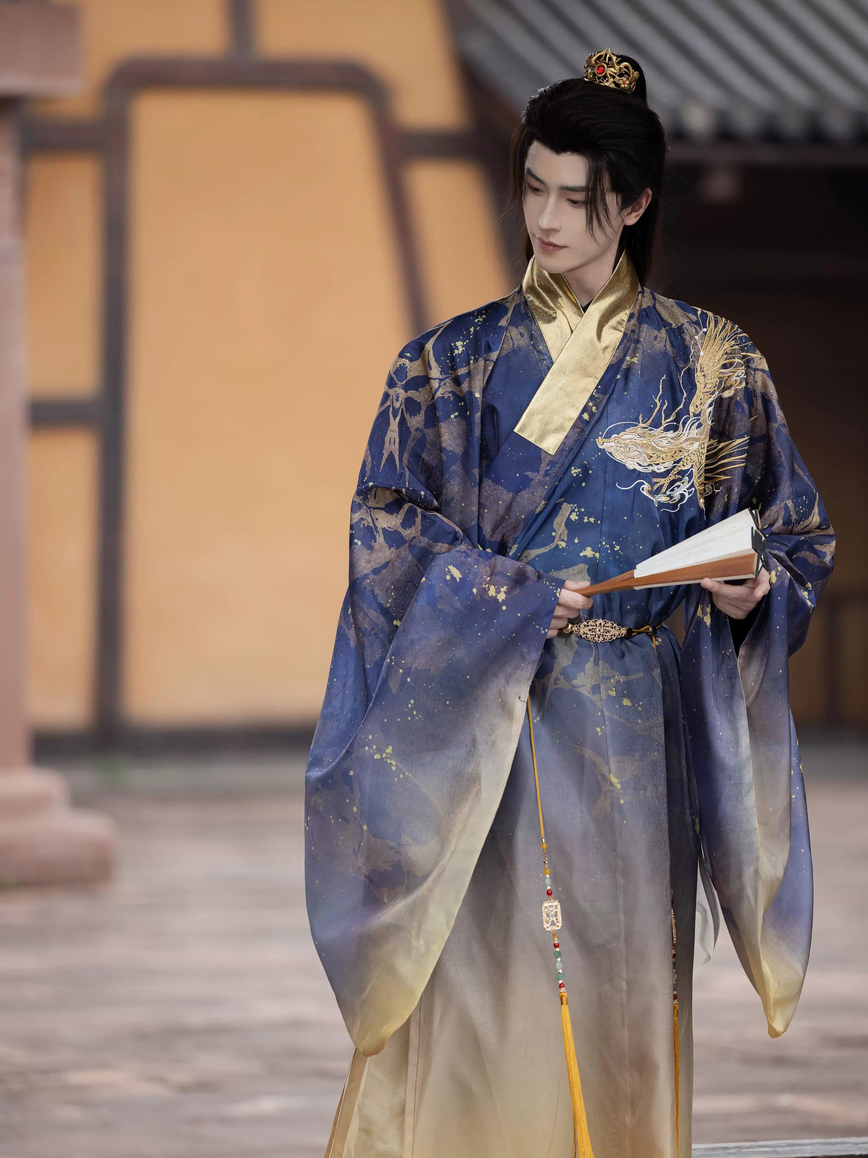 Ming blue Dragon Roar Hanfu robe with gold embroidery, worn by a model holding a book, exuding historical elegance and cultural charm.