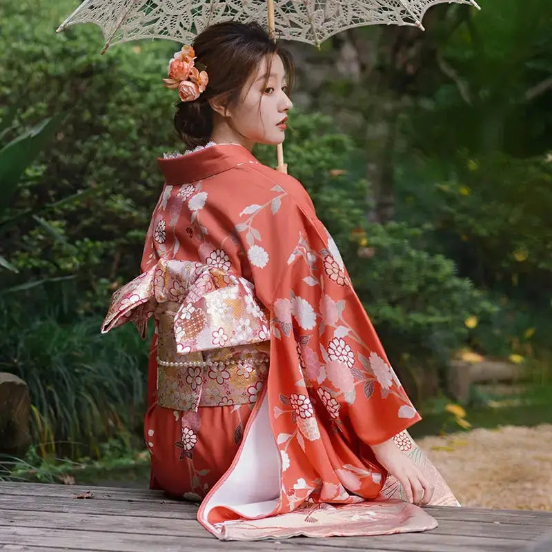 Back view of an orange chrysanthemum-patterned kimono with intricate obi detail, styled for photography in a serene outdoor setting.