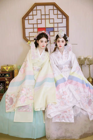 Two brides in Muzhi Korean embroidered wedding dresses, highlighting delicate floral embroidery and pastel accents for a regal wedding style.