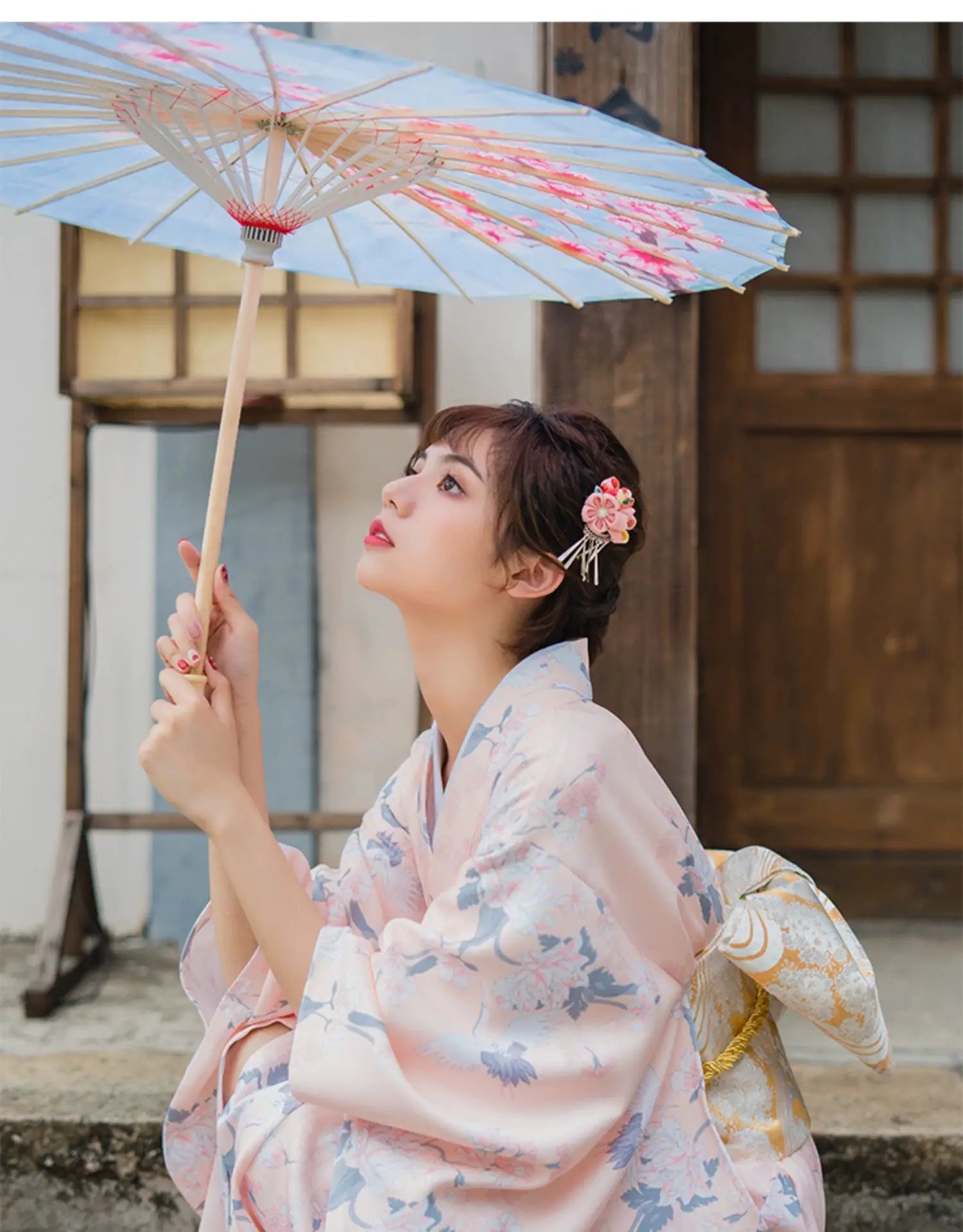 Woman in a pink yukata kimono with crane motifs, holding a parasol, showcasing a blend of traditional and literary Japanese style.