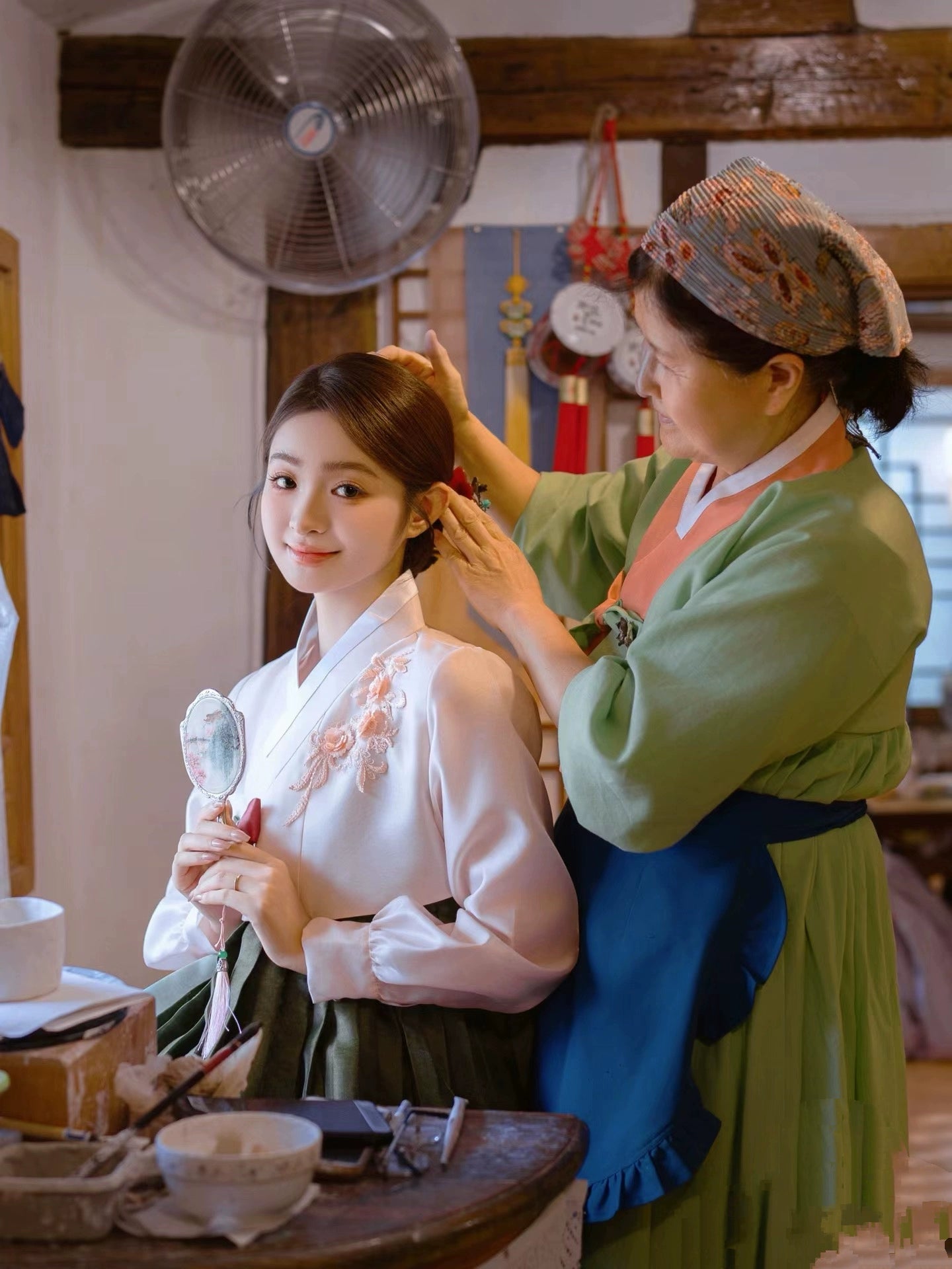 Green Korean hanbok being styled by a woman in a traditional setting.