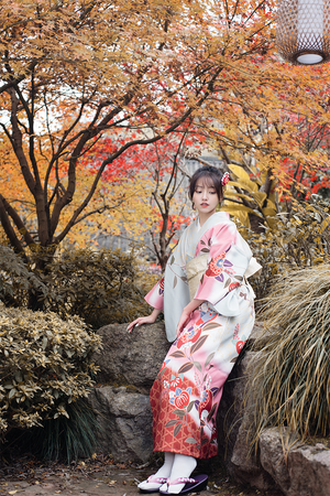 Traditional pink floral kimono worn in a garden with autumn trees and rocks.