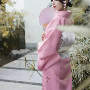 Back view of a pink Japanese kimono yukata with intricate floral details, complemented by a white obi and traditional fan.