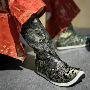 Side view of black and gold embroidered Dragon boots with a curved sole, paired with a red Hanfu robe, inspired by Ming-dynasty fashion.