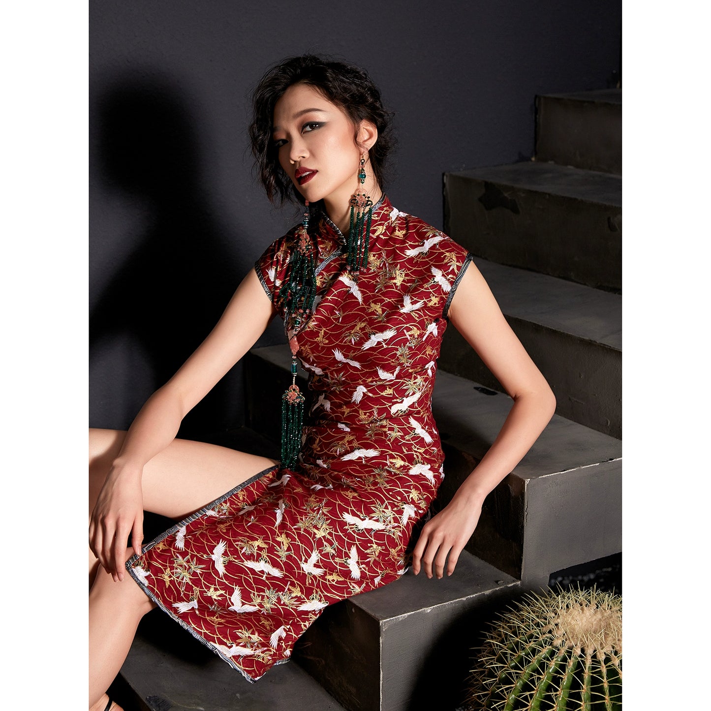 Model seated in red cheongsam with crane print, styled with statement earrings.