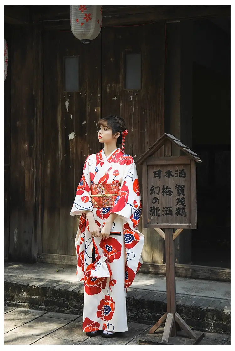 Elegant white and red floral Japanese kimono dress with wide sleeves, styled with a matching obi belt, worn in a traditional outdoor setting.