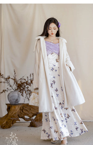 Model wearing a white fur jacket layered over a butterfly-printed fishtail skirt with a purple velvet bodice for winter fashion.