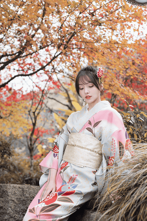 Close-up of pink Japanese yukata with gold obi, surrounded by autumn leaves.