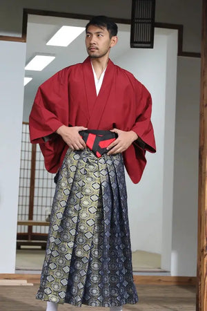 Close-up of a man in a Japanese traditional samurai costume with a red kimono and brocade skirt, standing in a traditional interior setting.