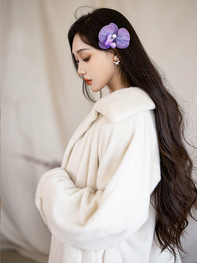 Close-up of a white eco-friendly fur jacket with a soft texture, styled with a purple floral hair accessory.