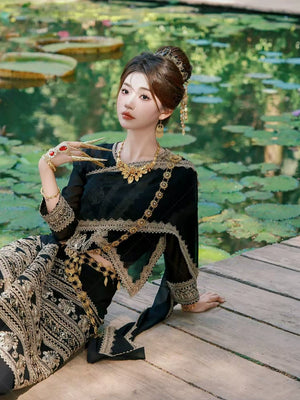 Model in Black&Gold Dai clothing female princess outfit reclining by lotus pond, showcasing full ethnic attire and accessories.