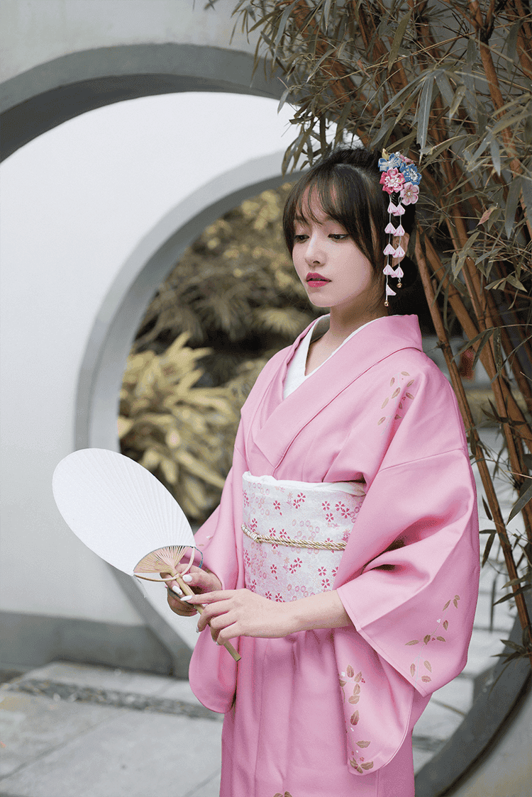 Close-up of a pink Japanese kimono yukata with floral patterns, accessorized with a fan and traditional hair ornaments.