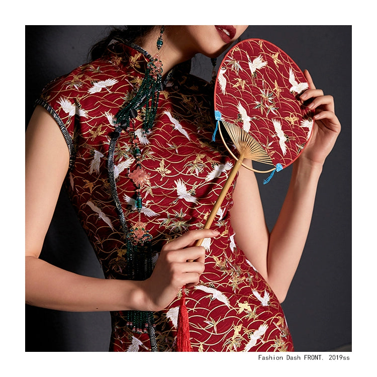 Detailed close-up of red cheongsam with crane print and traditional fan.