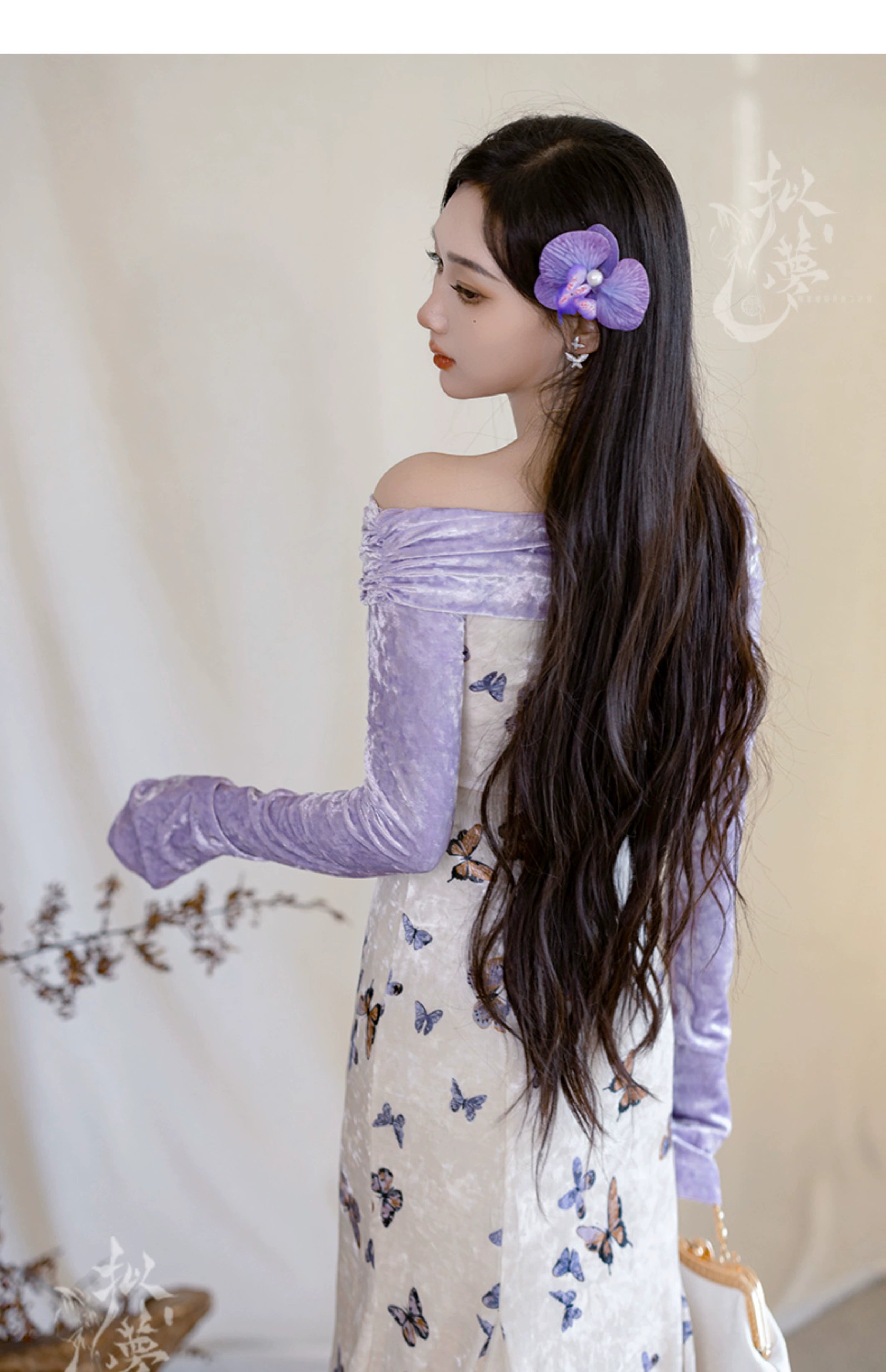 Back view of a model wearing a purple velvet off-shoulder top and butterfly-printed fishtail skirt, styled with long flowing hair.