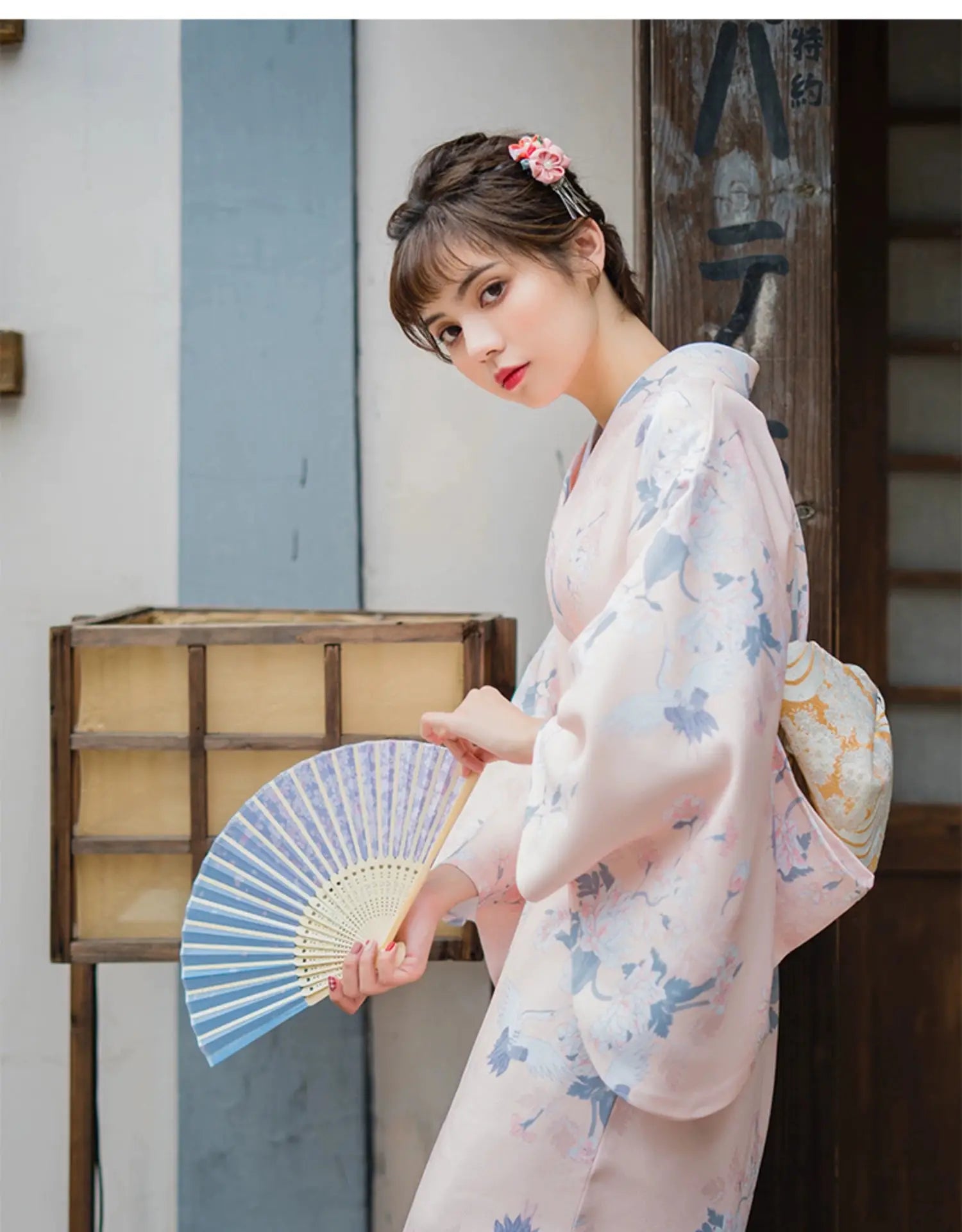 Woman in a pink yukata kimono with crane motifs, holding a fan, showcasing a refined and literary Japanese retro style.