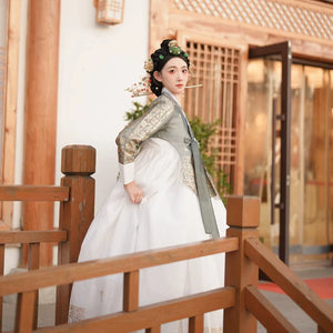 Korea Princess Hanbok with green top and white skirt on a wooden balcony.