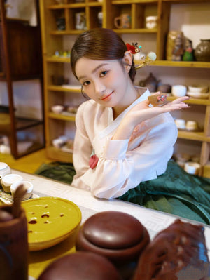 Green Korean hanbok displayed in a traditional tea room with cultural decor.