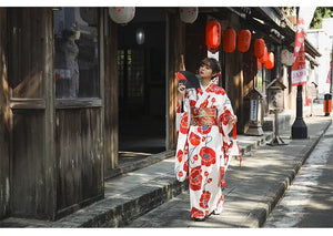 Woman walking in a white and red floral Japanese kimono dress, styled with an obi belt, in a traditional Japanese street setting.