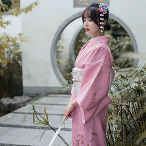 Side view of a pink Japanese kimono yukata featuring delicate floral designs, paired with a white obi and fan, ideal for retro-themed occasions.