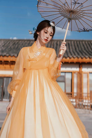 Elegant orange Yanbian Yanji Korean Hanbok dress with delicate embroidery, worn by a woman holding a traditional parasol in a historical courtyard.