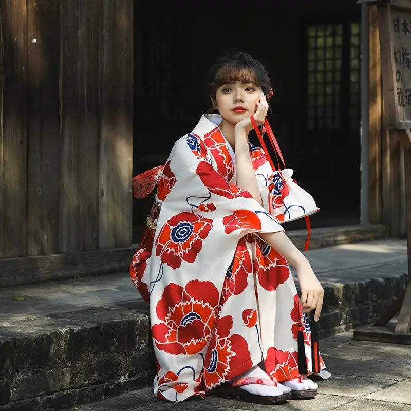 Woman wearing a white and red floral Japanese kimono dress, sitting outdoors with a thoughtful expression, showcasing the intricate design.