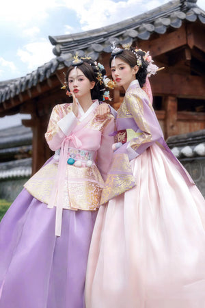 Two women in pink and purple Hanbok standing in front of traditional Korean architecture.