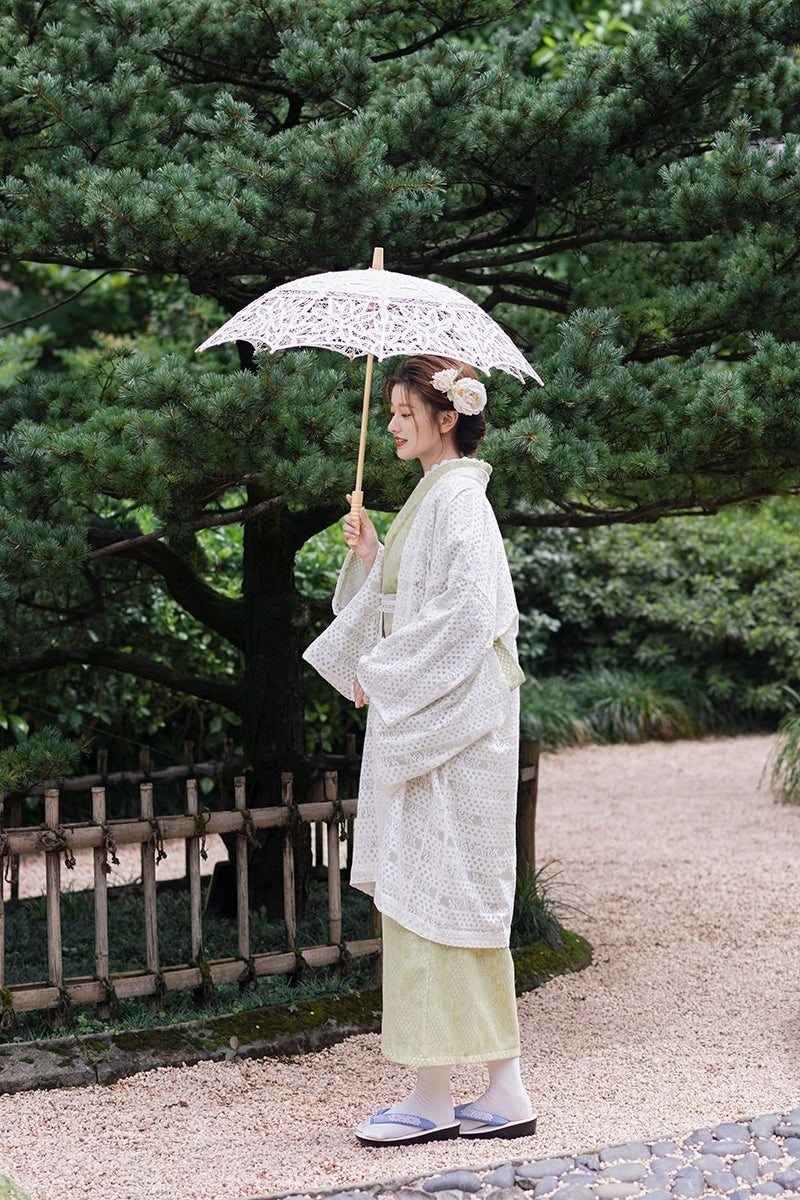 Full view of green kimono dress with lace parasol in garden.