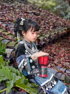 Girl in Miao blue Dai dance costume holding red drum, featuring intricate silver jewelry and ethnic embroidery for cultural performances.