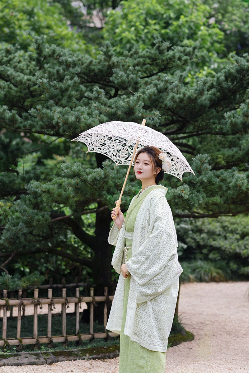 Model posing with lace parasol in green kimono dress outdoors.