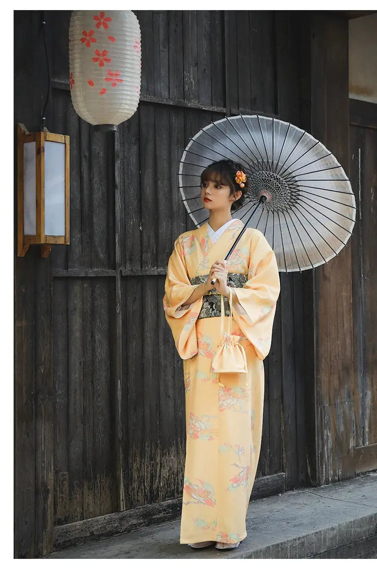 Woman in a retro orange Japanese kimono-style yukata with floral patterns, holding a black umbrella in a traditional wooden setting.