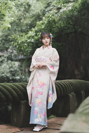 Model in a white Japanese kimono with floral designs, standing on a mossy bridge.