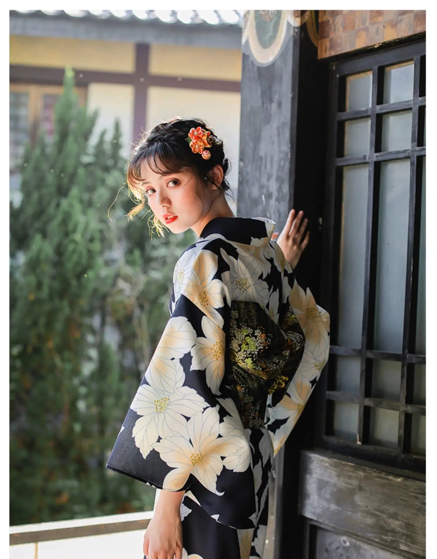 Woman in a Japanese kimono dress with a floral design, standing near a window, styled with a decorative obi belt.