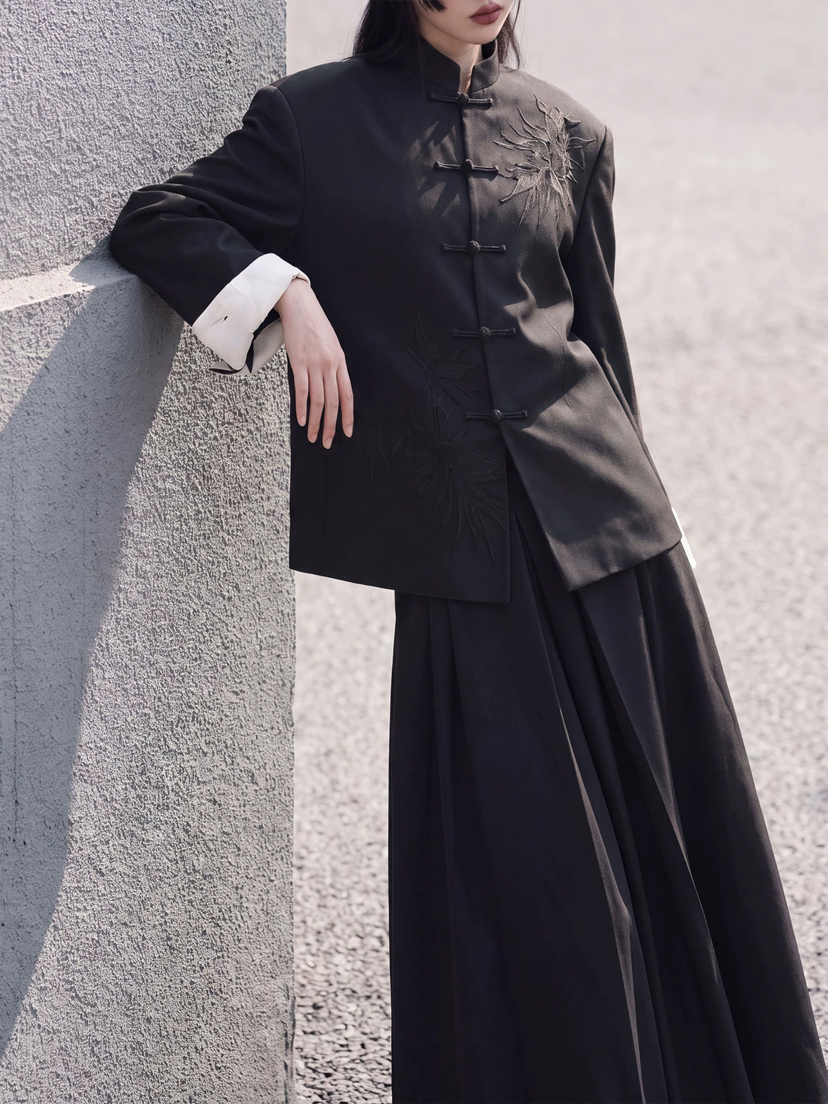 Black stand-collar blazer styled with a long skirt beside a wall