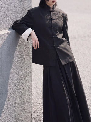 Black stand-collar blazer styled with a long skirt beside a wall