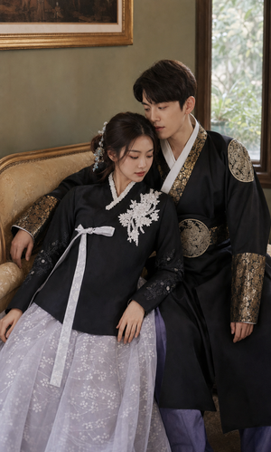 Vintage sofa lifestyle photo of dark Yanji couple hanbok with corrected longer women's black jeogori and men's gold brocade robe
