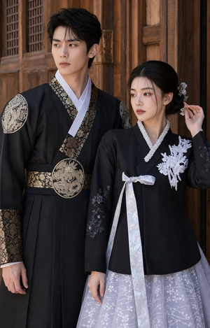 Close editorial view of dark Yanji couple hanbok with men's gold brocade robe details and women's white floral embroidered black jeogori