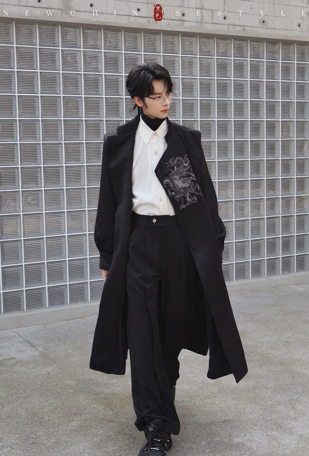 Black long coat with dragon embroidery worn open on a male model over a white shirt and black trousers for a contemporary Chinese style outfit.