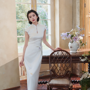 Full-length white floral bridal cheongsam beside a wooden chair