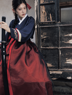 Navy jeogori and burgundy skirt detail beside a wooden door