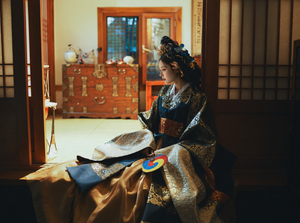 Navy and gold court-style Hanbok showing broad ivory-gold cuffs and gold skirt drape, seated side view