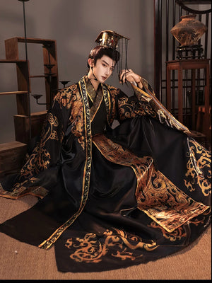 Seated view of a black and gold emperor Hanfu costume with wide sleeves and a trailing patterned hem