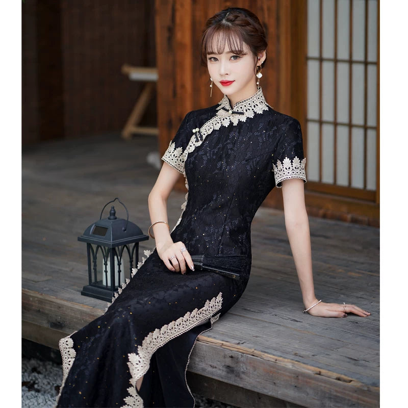 Seated view of the black lace cheongsam showing the fitted bodice and pale collar and sleeve trim