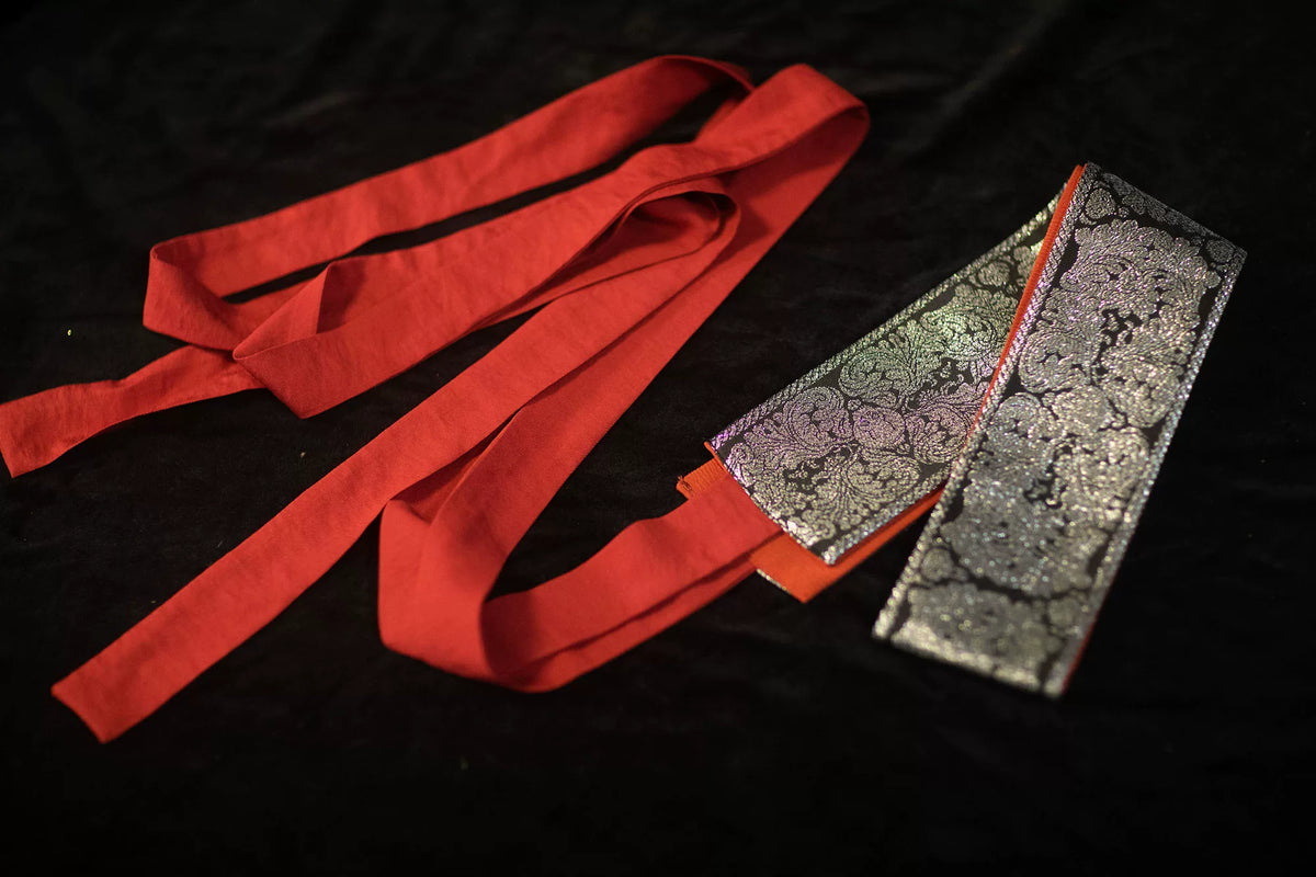 Single dark brocade sash with long red ties laid flat on a black background