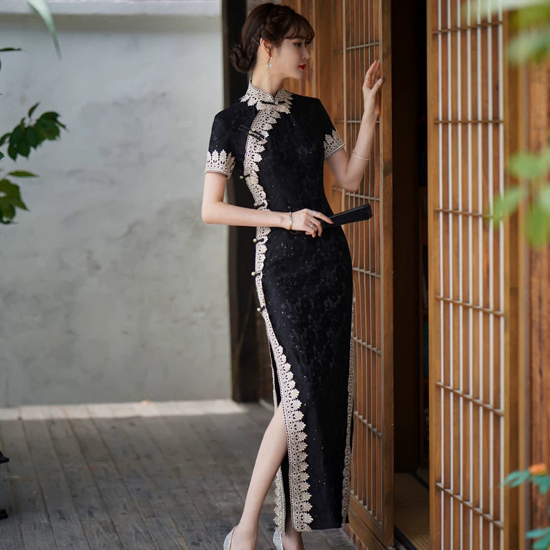 Side pose in a black lace qipao showing the fitted waist and high slit with pale trim